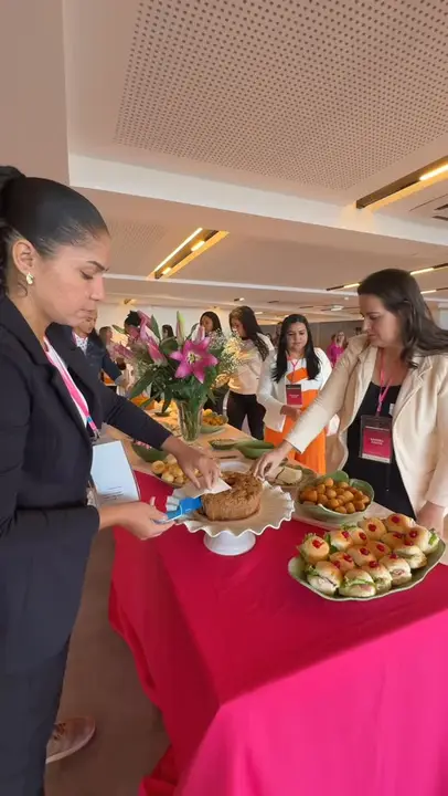 Participantes se servindo no coffee break, mesa com flores e salgados